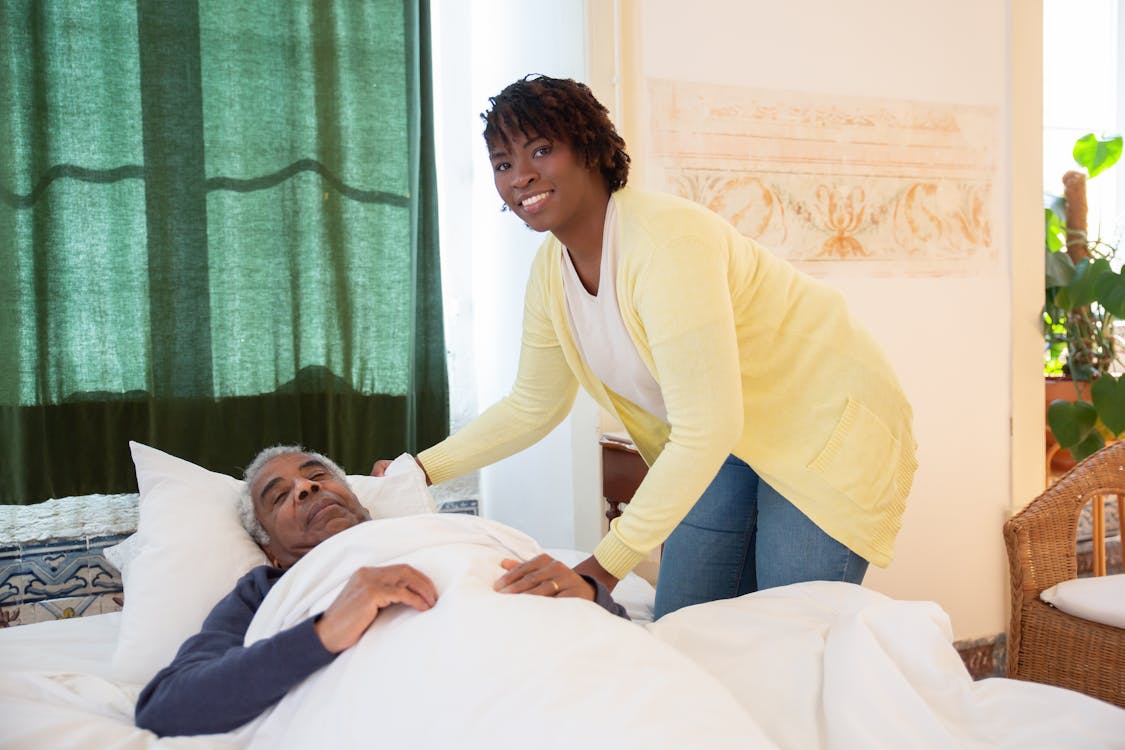 Caregiver tending to elderly man in a bright, warm bedroom
